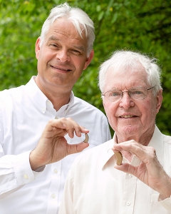 Unitron President Jan Metzdorff holding Moxi Kiss RIC (left); Unitron founding partner Rolf Dohmer holding a 205A BTE from 1966 (right).